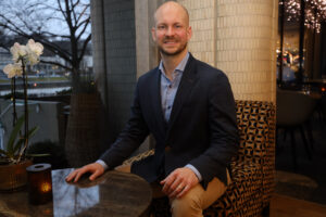 mies istuu tuolilla ja katsoo kameraan