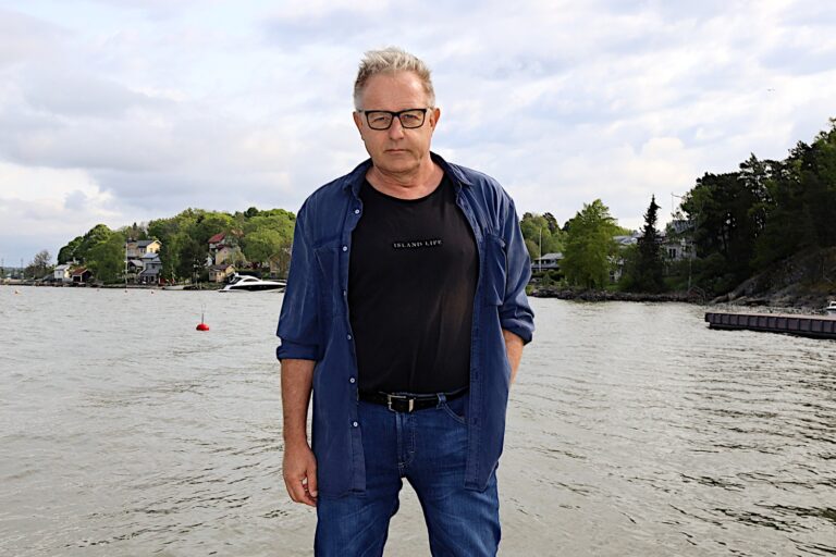 mies seisoo rannalla ja katsoo tuimasti kameraan