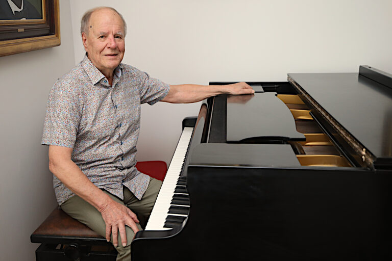 mies istuu flyygelin ääressä ja katsoo kameraan